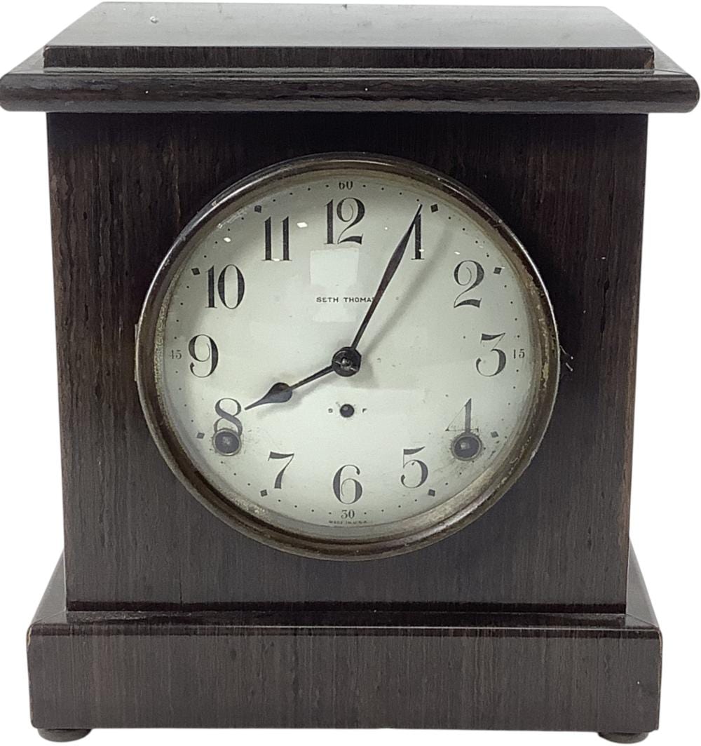 Front view of a vintage dark wood mantel clock with a round clock face and Roman numerals, showing clock hands and pendulum opening.
