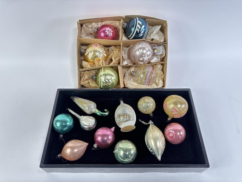 Assorted vintage-style round and shaped Christmas ornaments in a black display tray and cardboard box, with pastel pink, teal, gold, silver, and green glassy ba