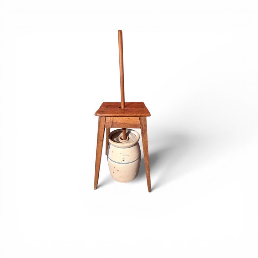 Wooden churn stand with a cream-colored stoneware churn vessel and a vertical dasher, photographed on a white background.