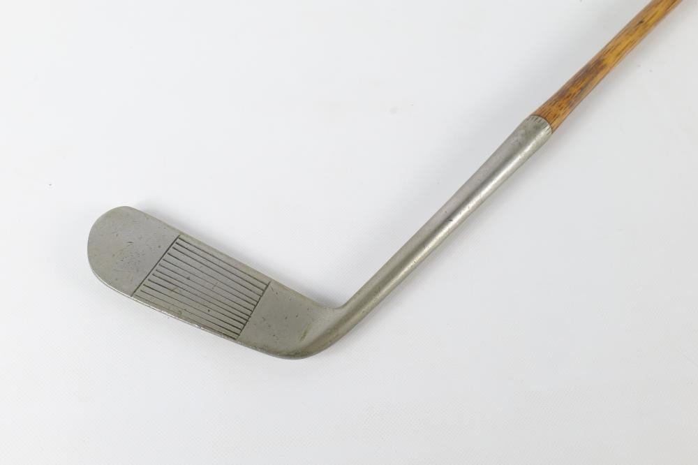 Golf club head and shaft shown against a white background, with a metal clubface and a light wooden grip.