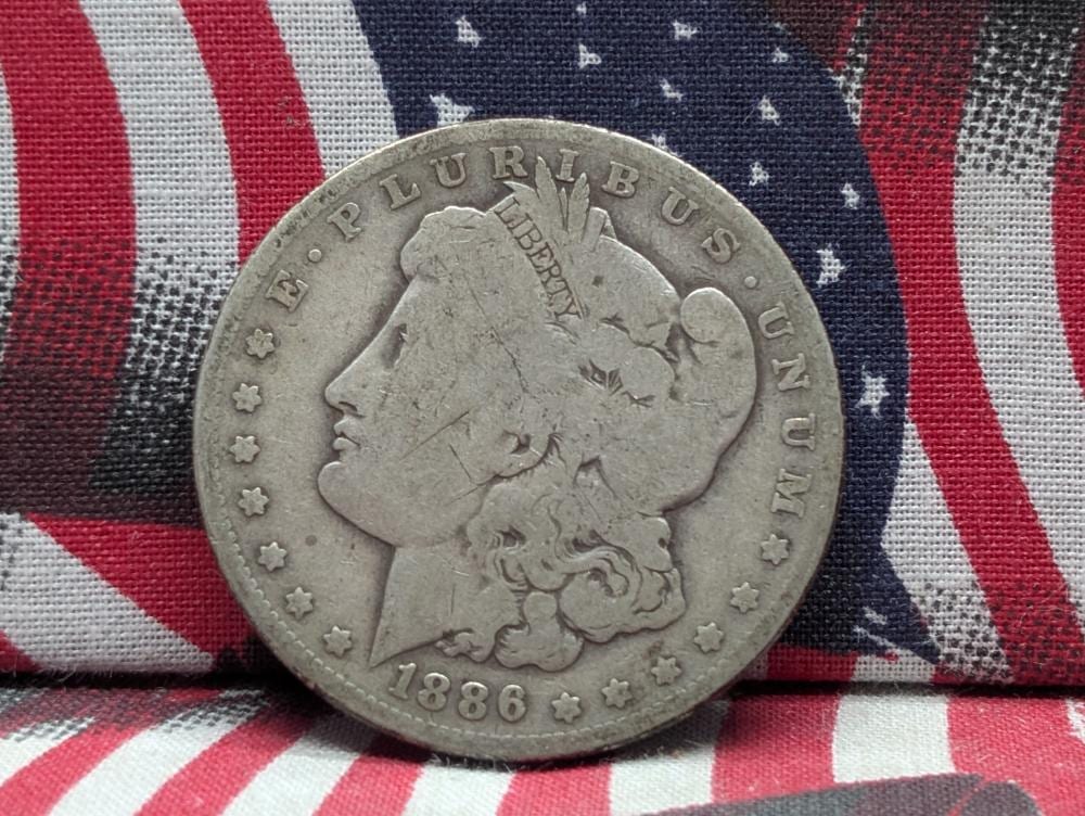 Silver coin with a left-facing portrait and the words “LIBERTY” and “1886” on a red, white, and blue striped fabric background.