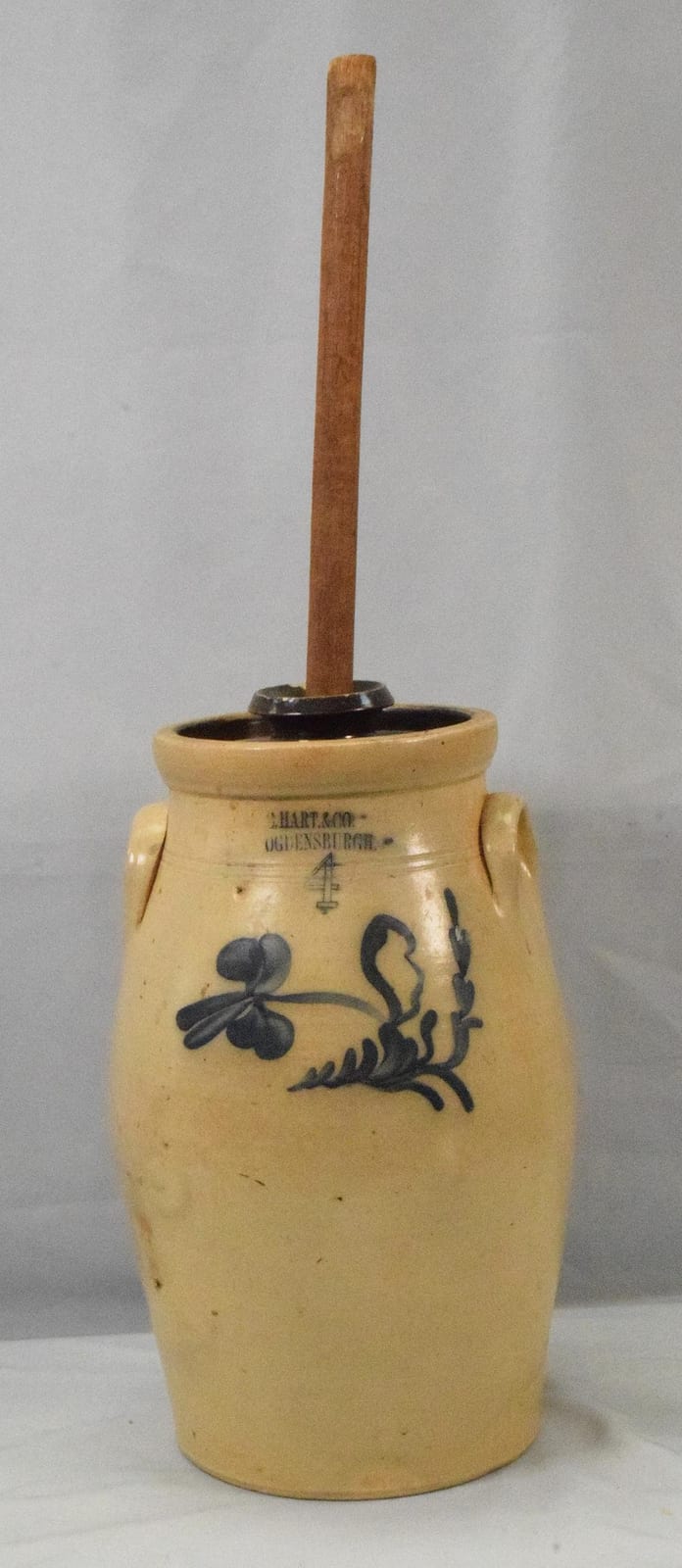 Small stoneware butter churn with a tall wooden plunger and cobalt-blue floral decoration on a cream-colored crock.