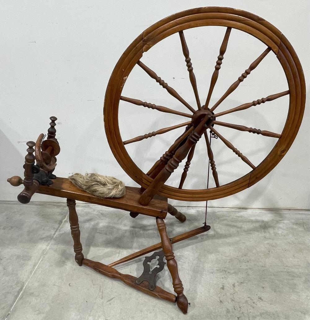 Antique wooden spinning wheel on a stand with a large wheel and spindle, plus loose fiber or yarn on the base.