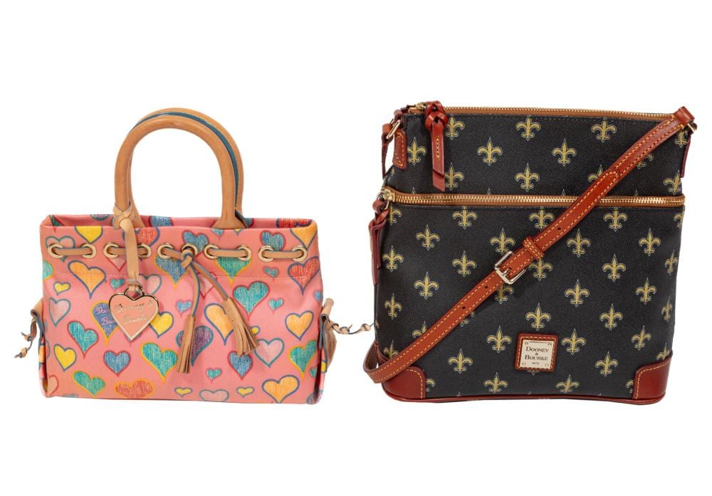 Two small crossbody/hand purses: one pink with colorful heart pattern and braided straps, and one dark brown with gold fleur-de-lis pattern and a brown cross-