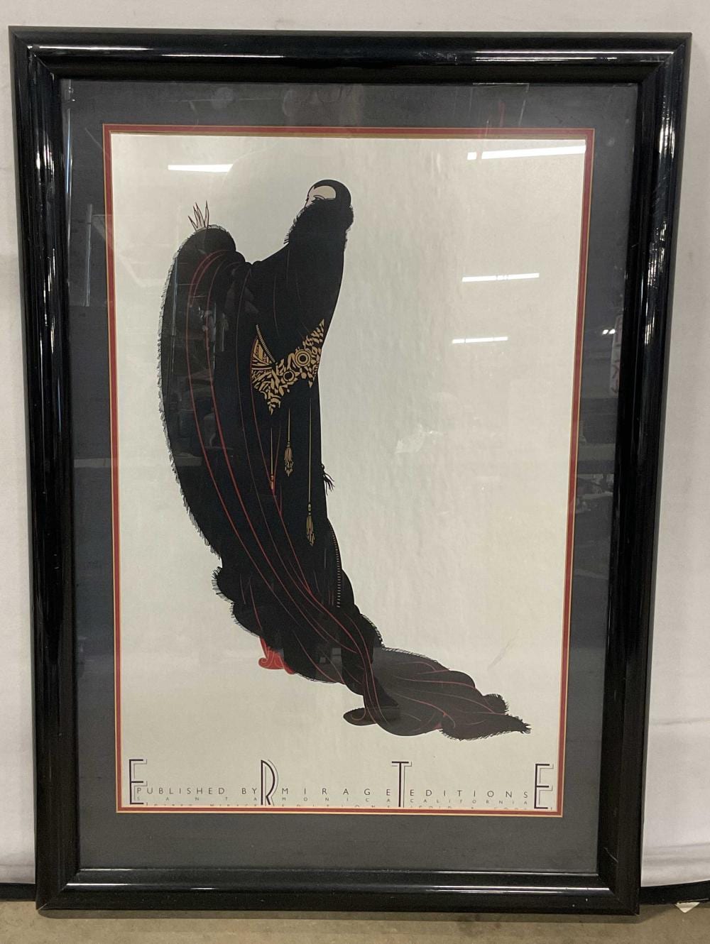 Framed Erte-style fashion figure silhouette print showing a seated dancer in black with gold and red detailing against a white background.