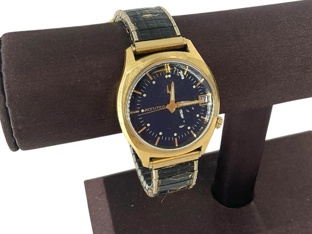 Vintage gold-tone wristwatch with black dial and gold hands, shown on a dark display cushion.