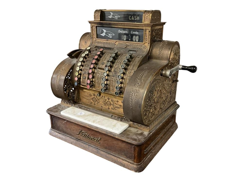 Vintage antique brass cash register with a digital display labeled “CASH,” coin slots, and engraved decoration on a wooden base.