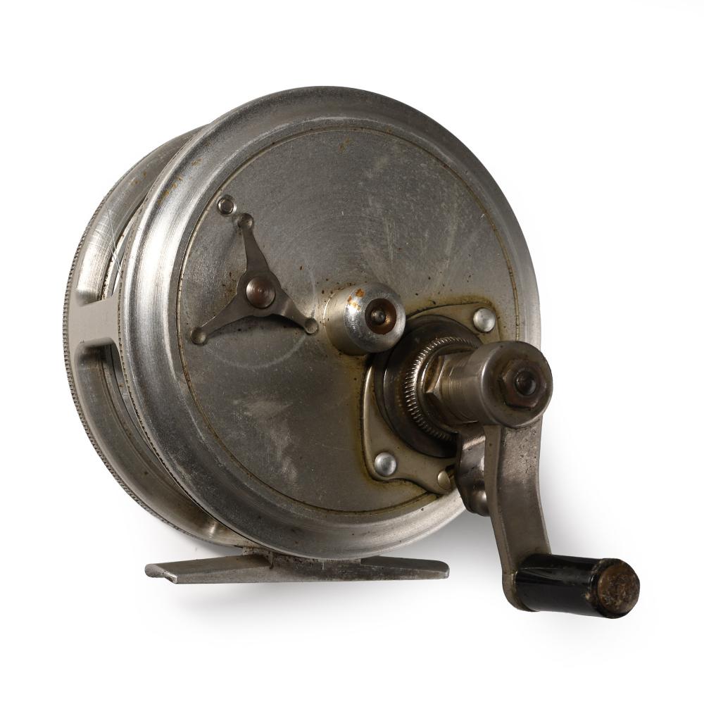 Close-up of a vintage metal fishing reel on a stand with the spool and handle visible.