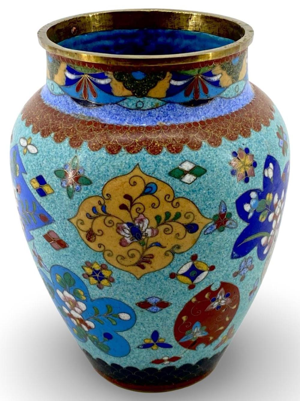 Close-up of an ornate blue enamel cloisonné brass vase with colorful floral and butterfly decorations and an open rim.
