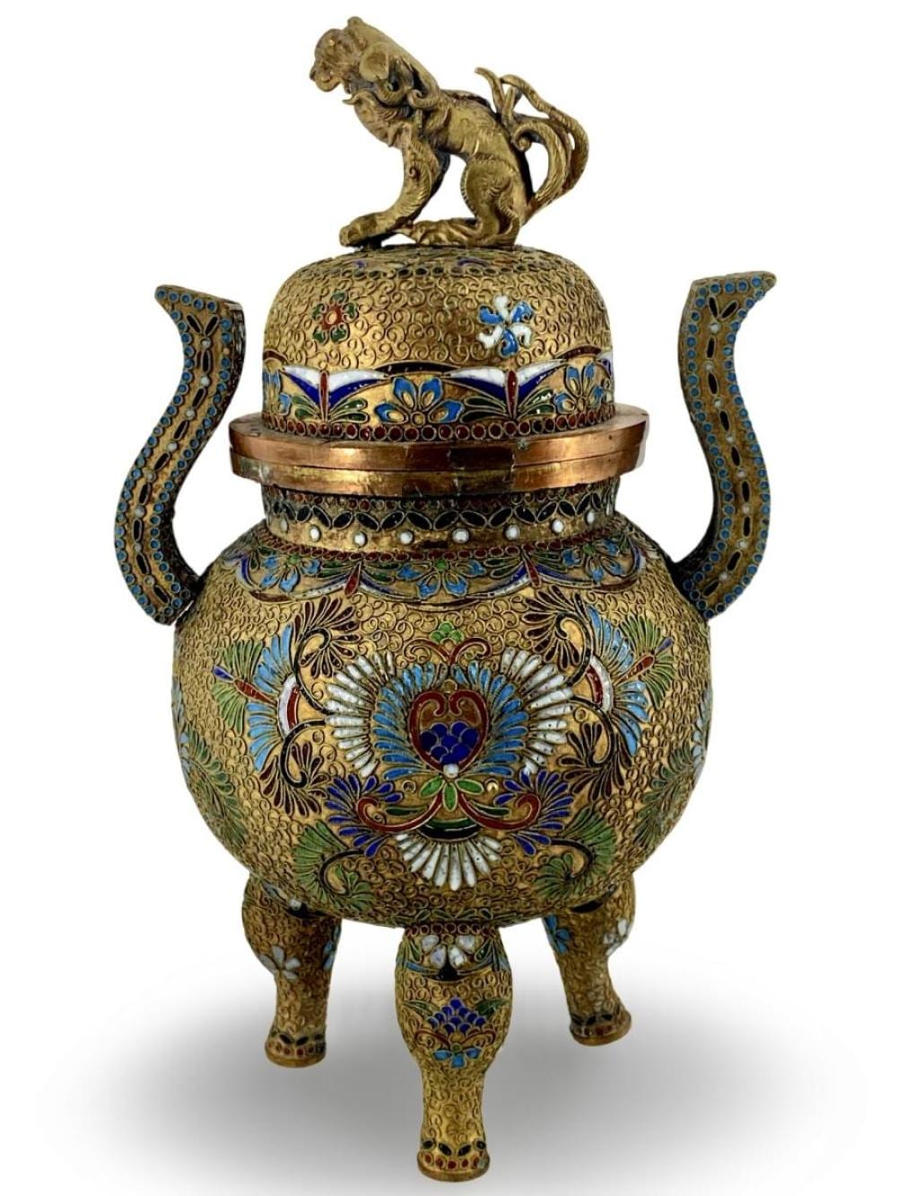 Vintage cloisonné enamel Chinese incense burner with a lidded body, curved handles, and a lion figure finial, decorated in blue, gold, and green.