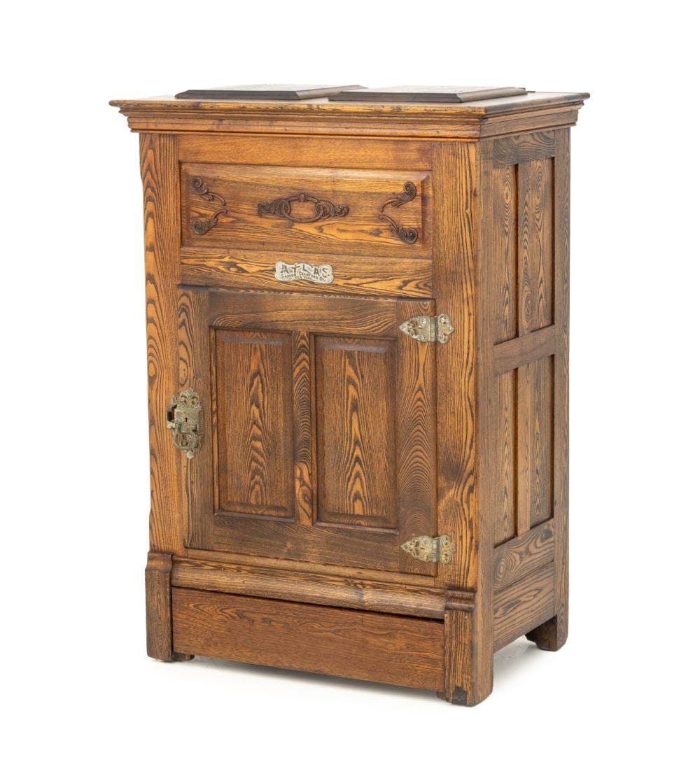 Wooden cabinet-style ice chest with a hinged front door, carved panel detail, and metal hinges, viewed from the front.