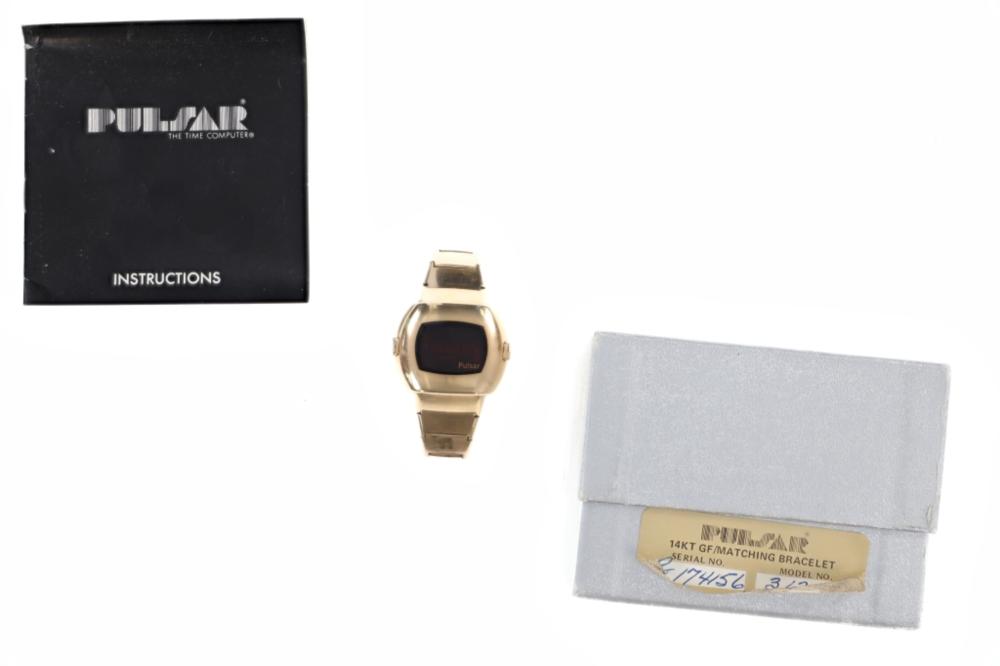Gold-tone wristwatch with a dark rectangular dial, shown with a black instruction booklet and a label in a box.