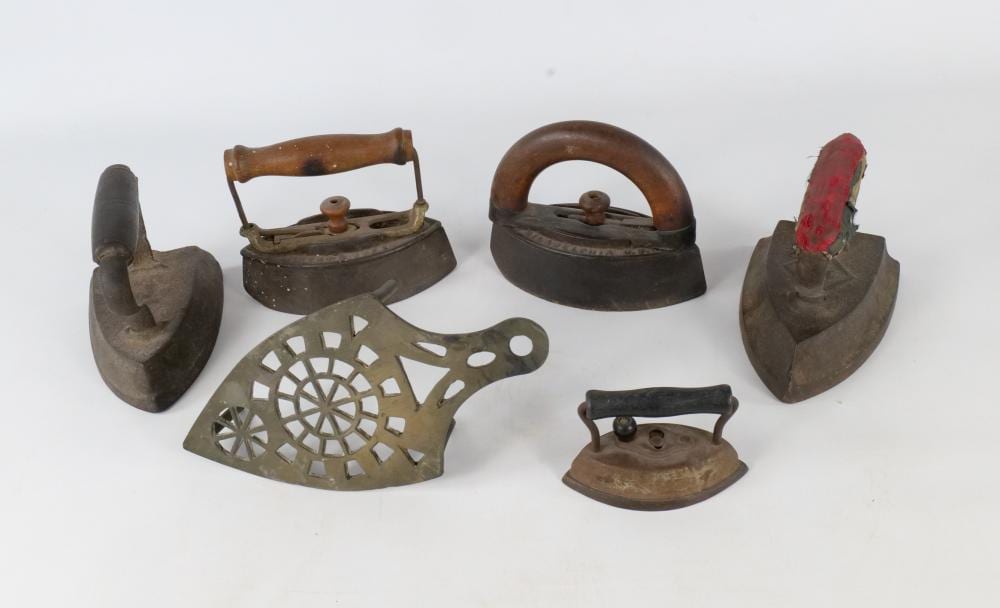 Set of five sad irons and one flat iron on a white background, including a pointed coal iron with red label marks.