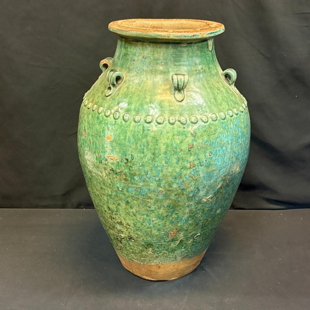 Green glazed ceramic martaban jar with a rounded body, short neck, ring handles, and speckled surface on a dark background.