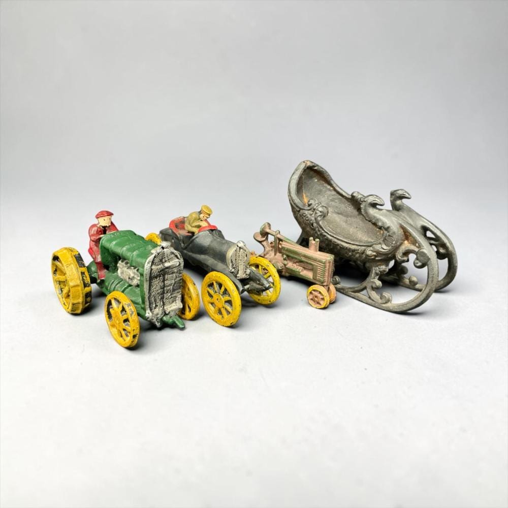 Colorful cast metal toy tractor pulling a wagon with small painted figures and a large silver plow-like attachment, on a white background.