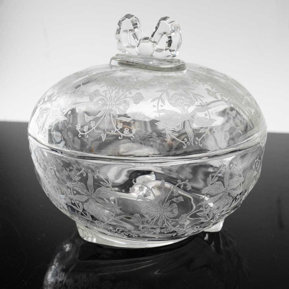 Clear glass covered candy dish with ornate etched floral and bird designs and a bow-shaped finial on top.