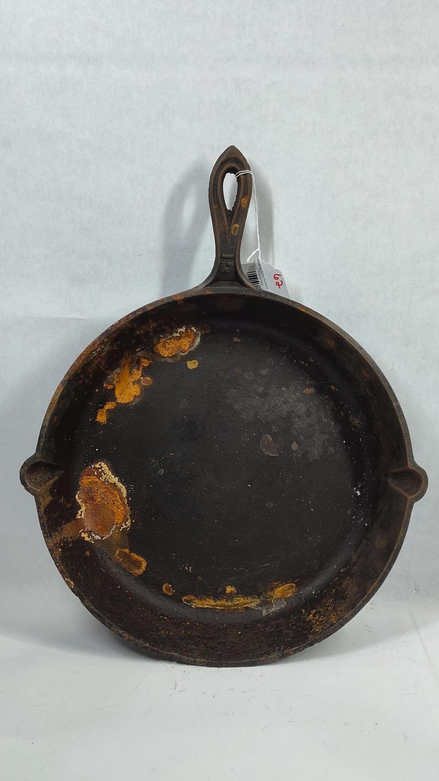 Round cast iron skillet with a curved handle and speckled dark interior, shown on a light background.