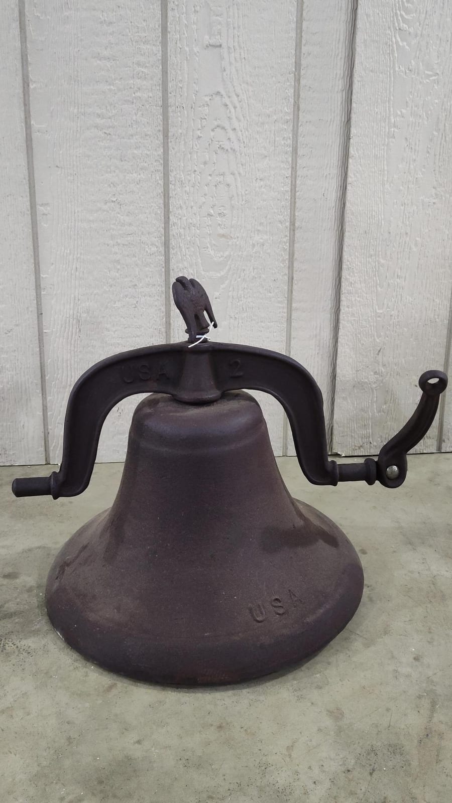 Cast iron farm bell with eagle-style finial and black mounting yoke, stamped with numbers on the bell body.