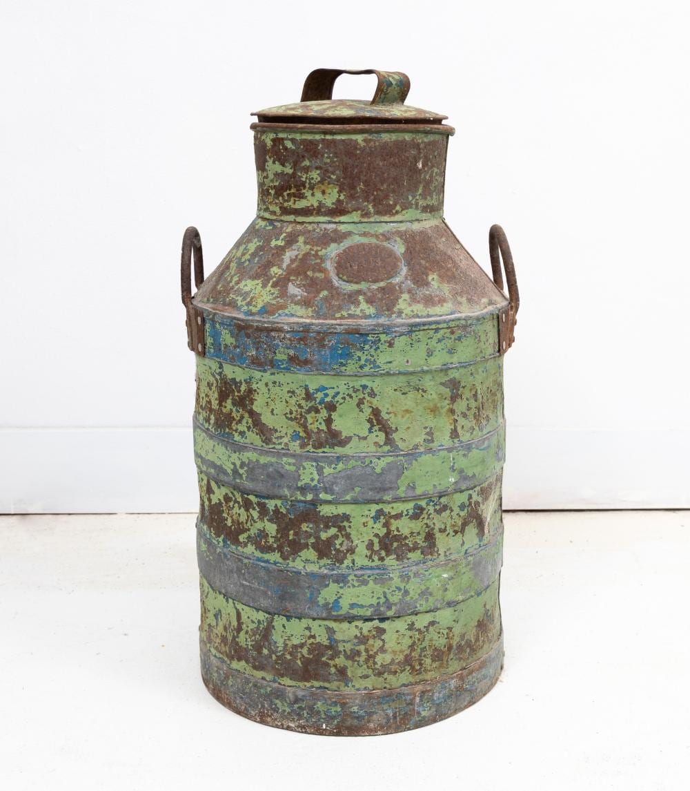 Vintage metal milk can with lid and side handles, showing worn green-blue patina and flaking paint.