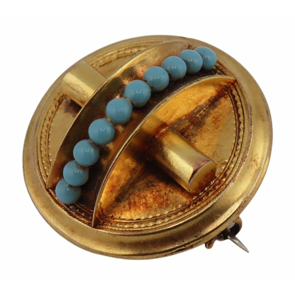 Close-up of a gold-tone Victorian-style brooch with a curved blue enamel bead-like band and brass-colored pin back.