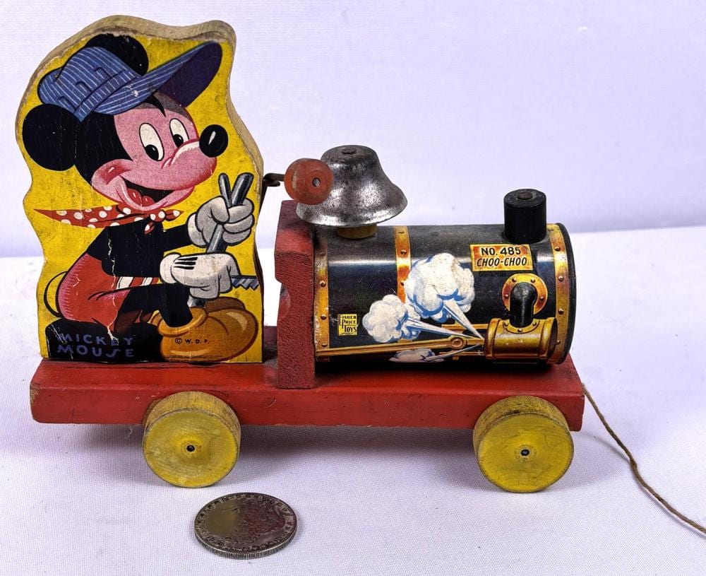 Vintage pull-along toy train with Mickey Mouse image on a yellow card, metal bell and wheels on a red wooden base.