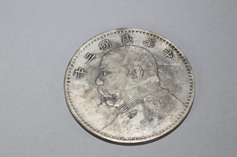 Silver-colored round coin with a raised profile of a man and Chinese-style characters around the rim.