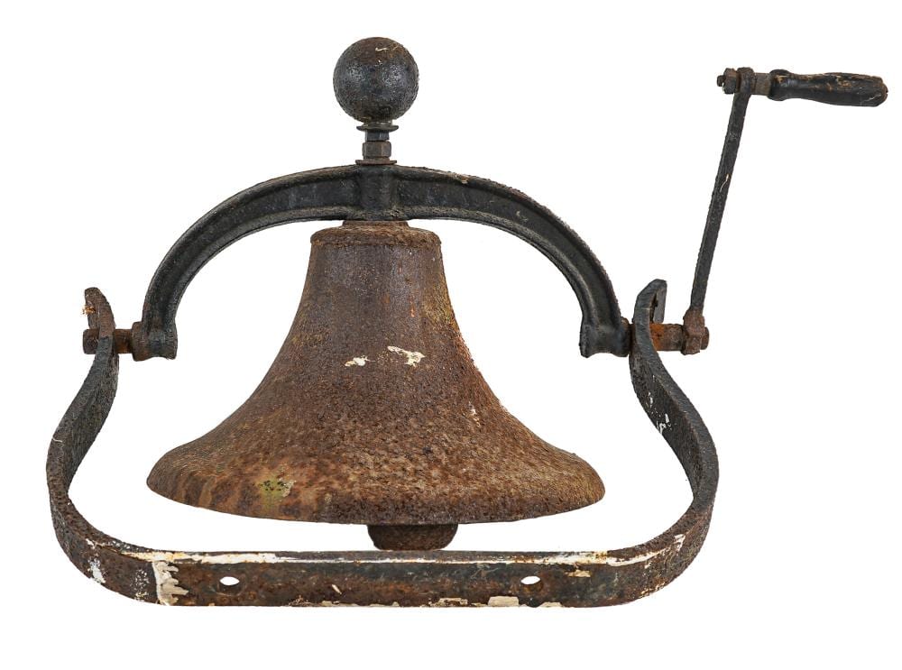 Rusty cast metal farm bell with arched handle and hanging striker, photographed against a white background.