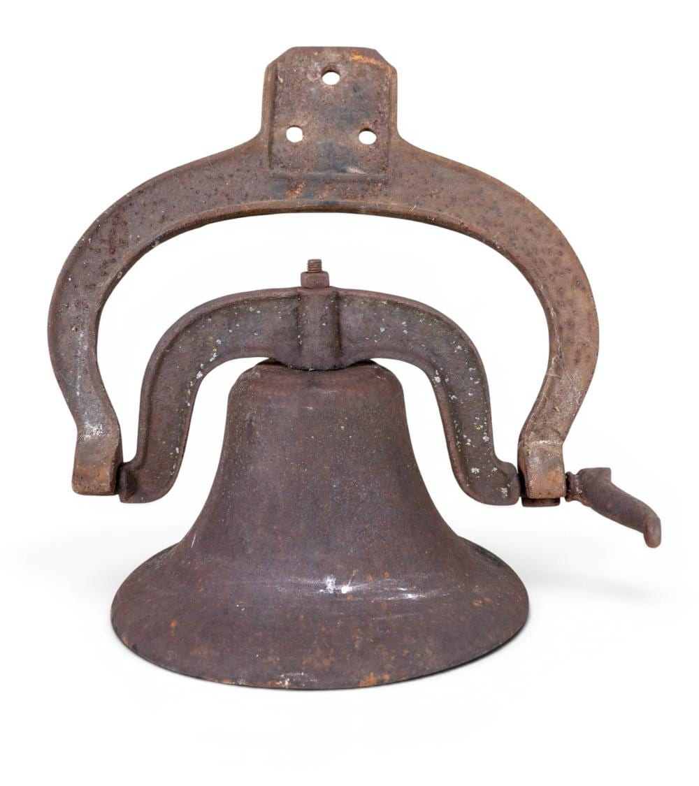 Rusty cast iron farm bell with arched handle and clapper visible, photographed against a white background.