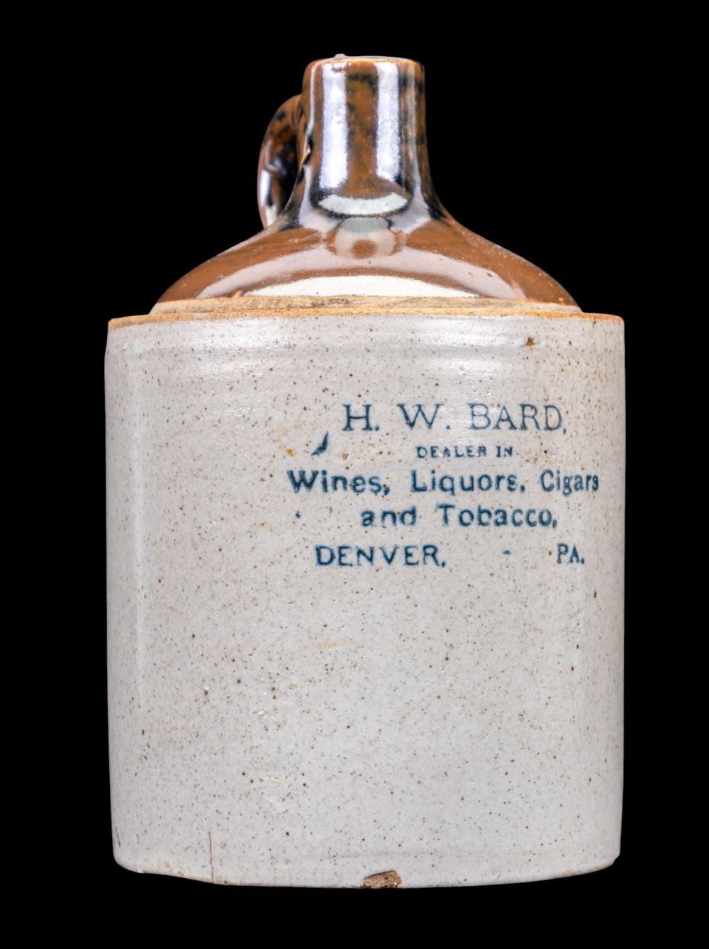 Brown-glazed stoneware whiskey jug with a white label band reading “H. W. BARD” and “Dealer in Wines, Liquors, Cigars and Tobacco.”