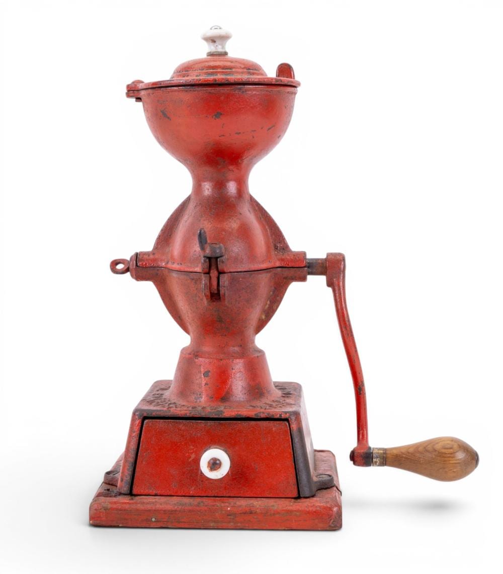 Red cast iron hand-crank coffee grinder with a round hopper on top and a wooden handle on the side.