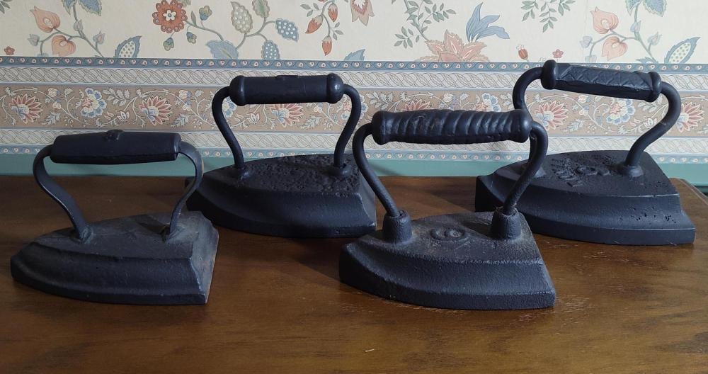 Three black cast-iron sad irons with curved handles placed side by side on a wooden surface.
