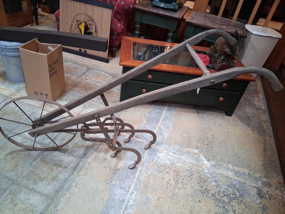 Old five-tine hand cultivator with wooden handle and metal frame on a worktable in a cluttered room