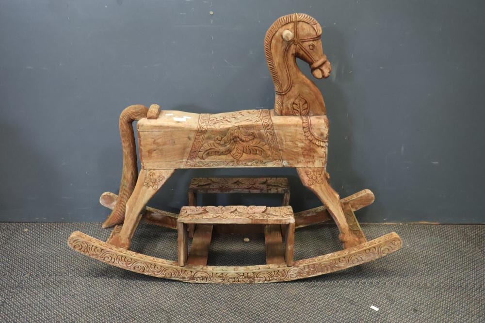 Carved wooden rocking horse with a brown horse head, arched back, and patterned wooden base on a dark surface.
