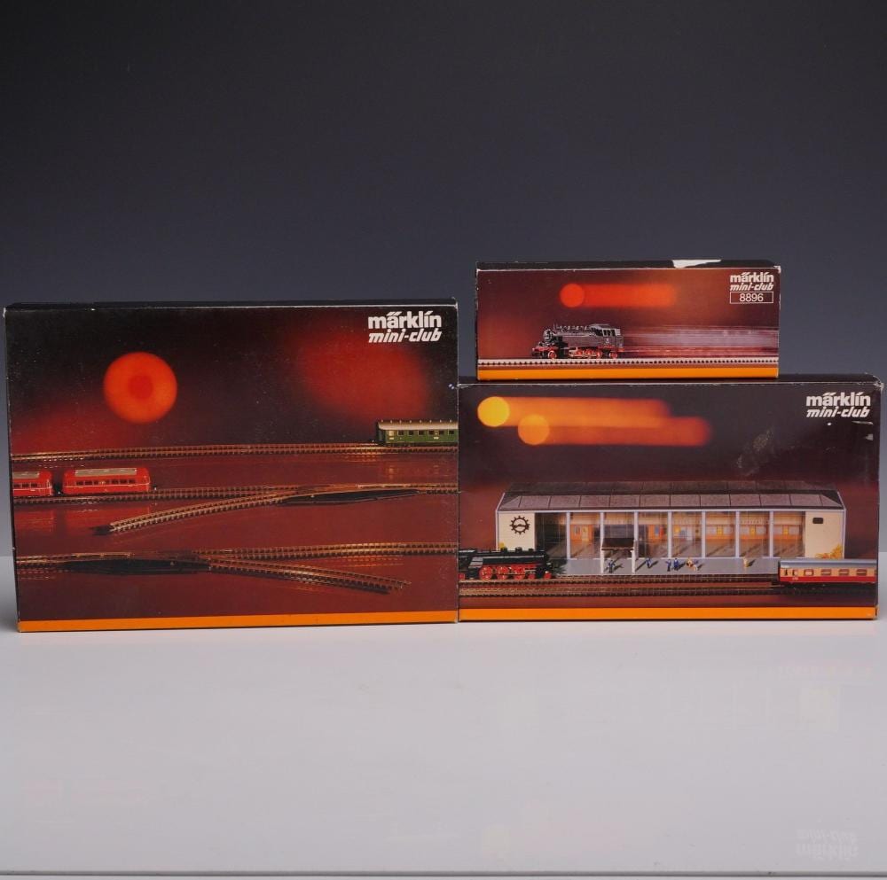 Boxed Marklin mini-club Z-scale model train sets with a tank locomotive and a station building, plus track pieces shown in packaging.