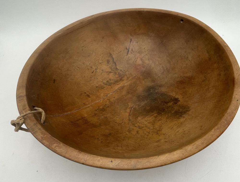 Round wooden bowl with a shallow rim and visible wear marks, photographed from above with a small handle-like protrusion on the left.