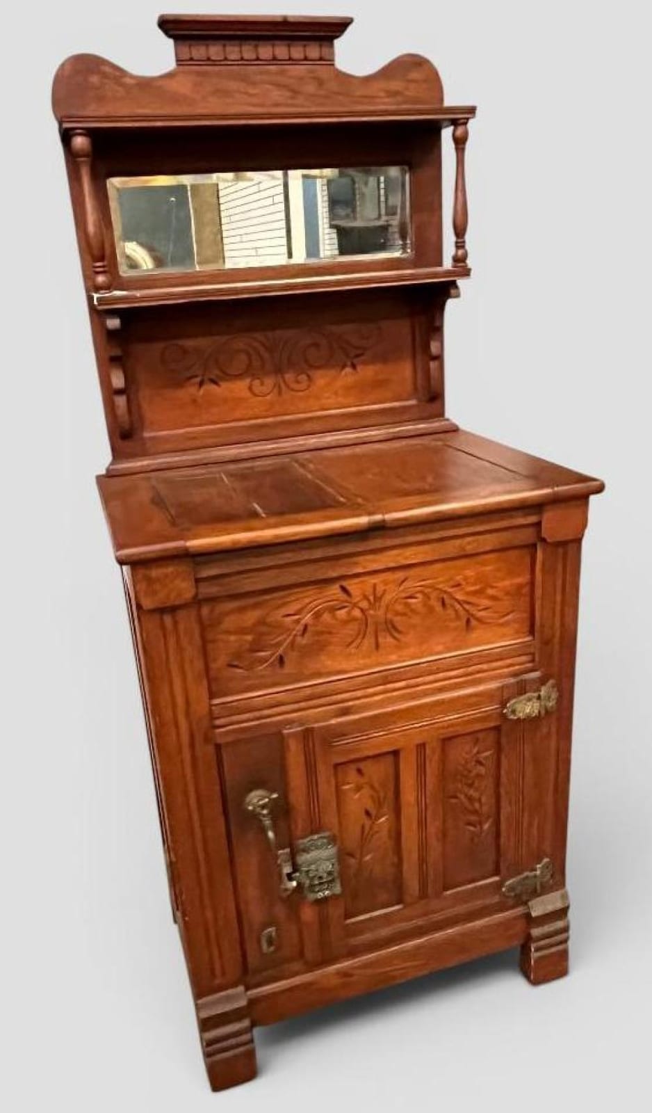 Wooden ice box or cabinet with a rectangular mirrored opening, carved floral design on the front door, and a raised top.