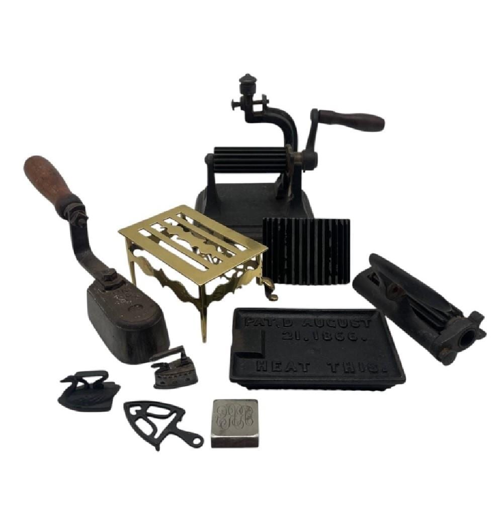 Set of antique cast iron sad iron and ironing accessories on a white background, including a press iron base and small irons/tools.