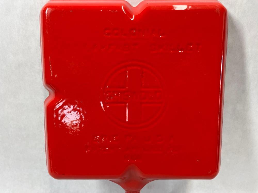 Red enameled cast iron skillet with a visible brand mark embossed on the center surface.