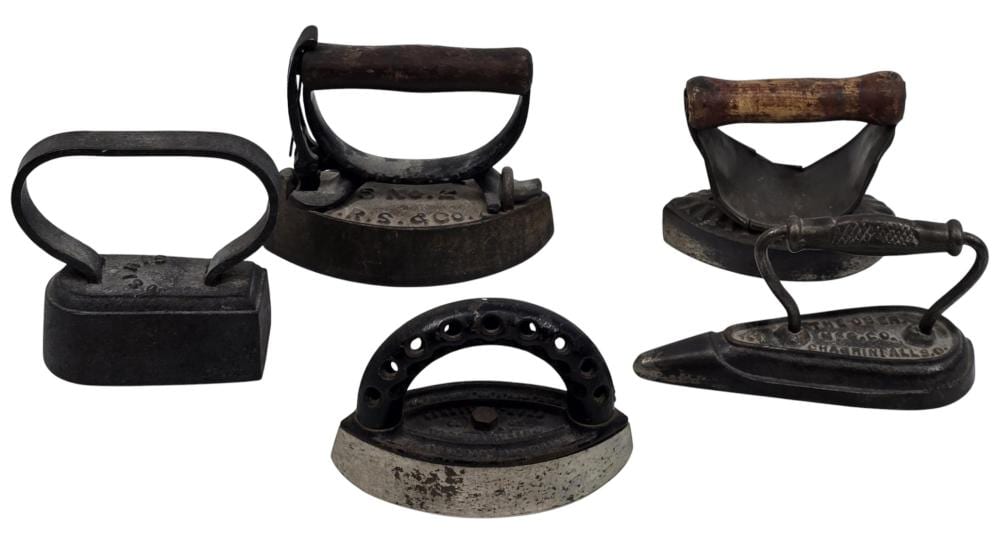Five antique cast iron sad irons shown together, each with a curved triangular sole and worn brown handles on a white background.