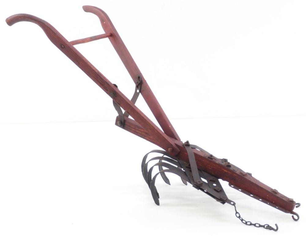 Wood-and-metal horse-drawn cultivator tool with curved frame, multiple tines, and a chain on the ground edge.
