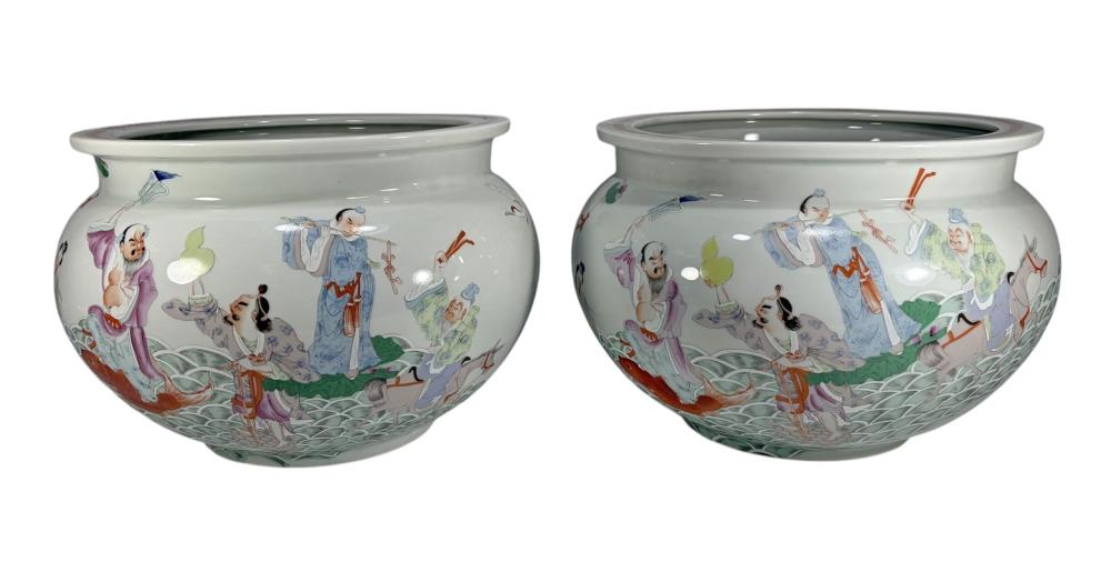 Pair of light-colored ceramic fishbowl jardinieres painted with figures in traditional clothing and pond/lotus motifs, with green rims.