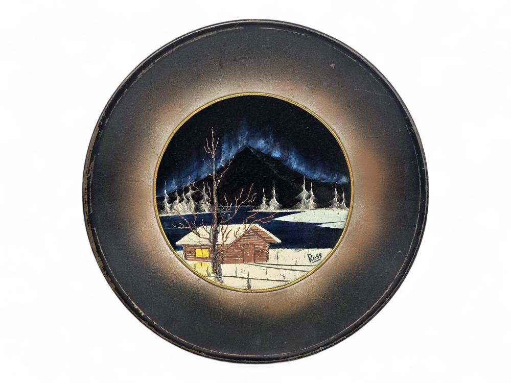 Framed painting circle showing a snowy winter cabin with a small porch, bare trees, and dark blue mountains under a dusk-like sky.
