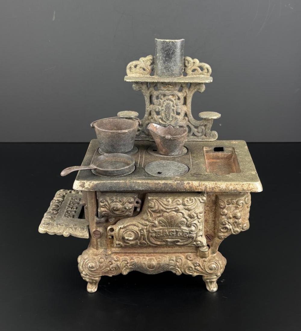 Cast iron toy stove with ornate scrollwork base, two small pots on top, and a central cylindrical chimney-like piece.