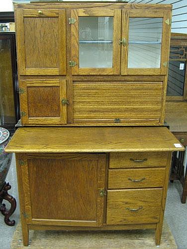 Wooden hoosier-style kitchen cabinet with a hinged top and drawers, shown front view with glass door and open work surface.