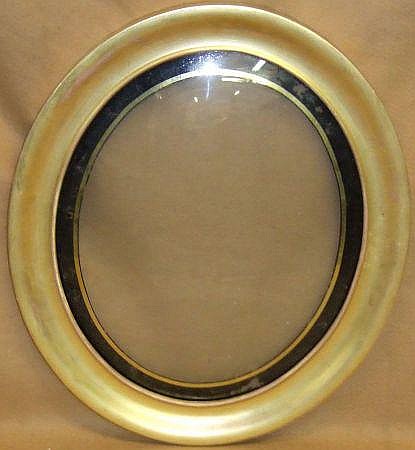 Close-up of a plain oval gold picture frame with a beige background and inner dark border.