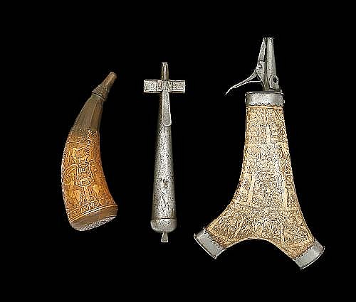 A group of three metal gunflask-style containers, including an upright powder-flask with engraved patterns, plus two matching conical pieces, shown against a黑背景