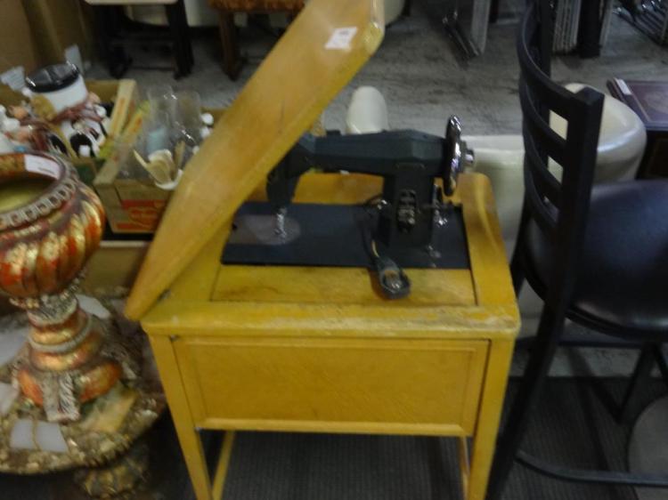 Yellow antique sewing machine on a stand, shown at an angle with a metal pedal and fabric table in view.