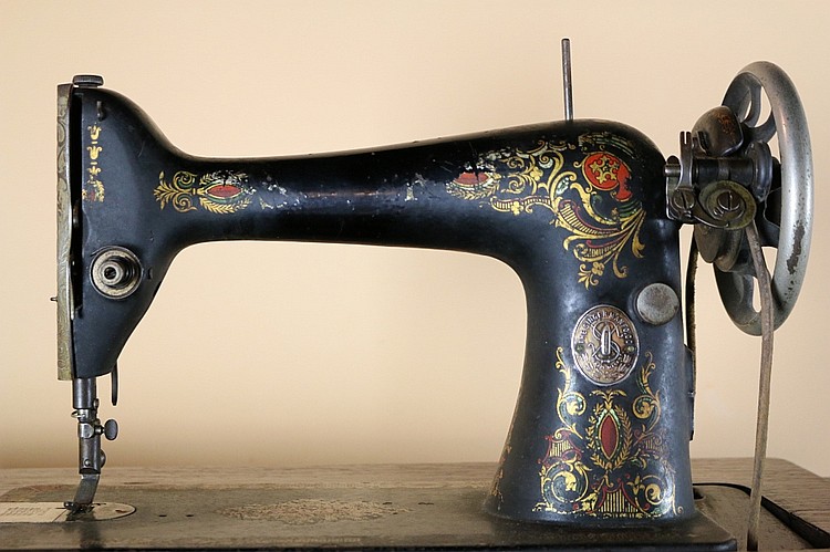 Antique blue sewing machine with gold floral scrollwork paint and an upright hand wheel, shown on a flat base.