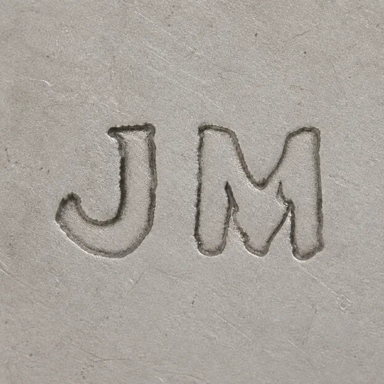 J M: The clearly supported J and M letterforms in left-to-right order with worn serif-like contour geometry and no decorative outer invention; oxidized reconstruction.