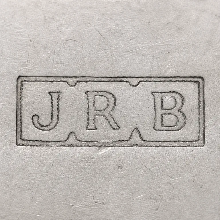 John Reginald Burrows: Unfilled long rectangular plaque with J-R-B sequence, nested irregular border details, and left-to-right layout; oxidized reconstruction.